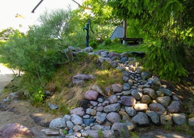 Wasserpsielplatz mit Kletterhügel aus Steinen sowie Rutsche und Pumpe