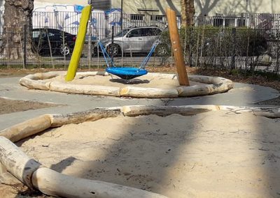Spielplatz mit liegenden geschliffenen Robinienstämmen eingefasst, sowie Nestschaukel